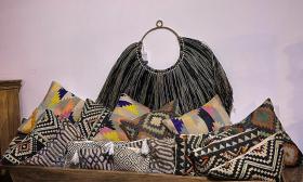 A pile of both muted and colorful kilim pillows, and a black and grey wall hanging from Artisan Furniture and Finds