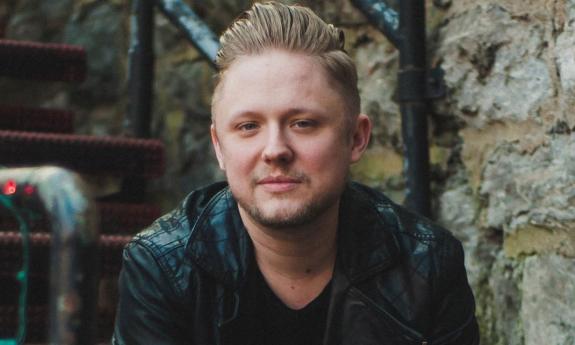 Singer/songwriter Tofer Brown headshot on stairs with rock wall in background.