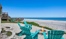 Four teal beach chairs around a fire pit, just off the beach and the Atlantic Ocean