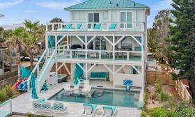 A white and teal beach house with a pool, and three levels with a deck