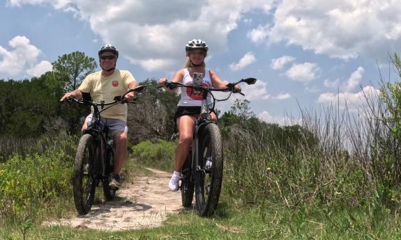 A couple on their e-bikes, on a sandy trail near the coast