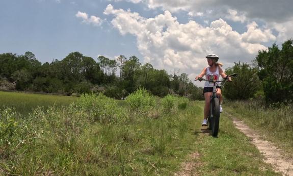 A woman biking on a trail, near the coast