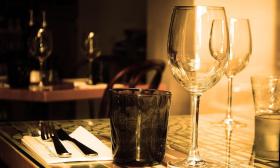 A table settign with wine glasses, in a dark bar with light coming through a window