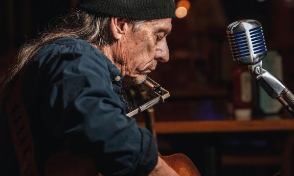 Denny Blue, with harmonica and guitar at a microphone