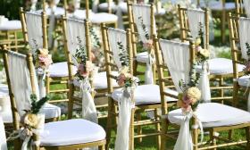 Rows of outdoor chairs with gold and white colors and simple floral attachment
