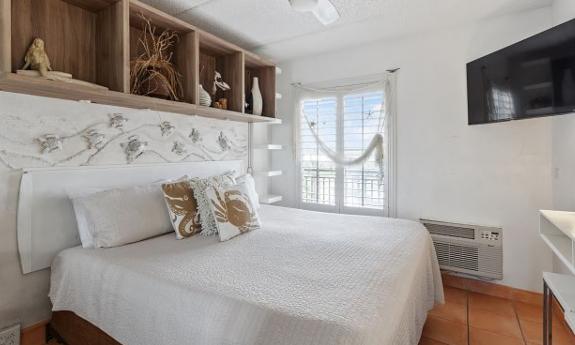 The bedroom in one of the balcony suites at Beacher's Lodge, with light, beachy decor and a flat-screen TV in the corner