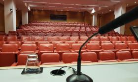 A view of an empty lecture hall with red chairs, as seen from the lectern