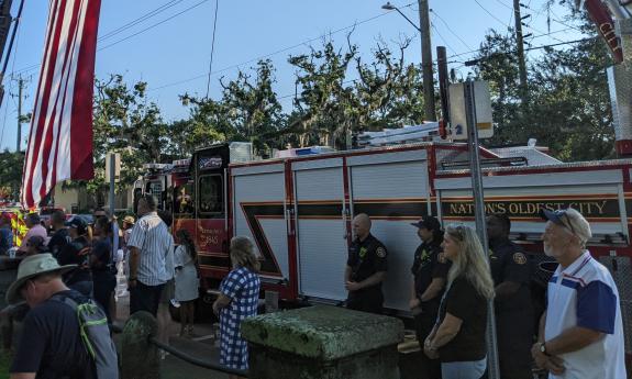 Members of the public stand near one of the ladder trucks holding a large American Flag during the 9/11 Remembrance Ceremony in St. Augustine