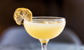 A cocktail, the "lavender bee's knees," botanical gin, honey syrup, and lemon juice, with a dried lemon slice for garnish