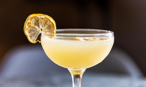 A cocktail, the "lavender bee's knees," botanical gin, honey syrup, and lemon juice, with a dried lemon slice for garnish