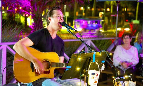 A male muisician, seated at a microphone outside at Salt Life Food Shack