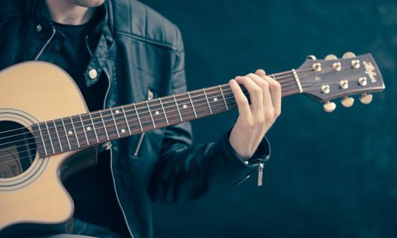 A guitarist, wearing a black leather jacket, playing an acoustic guitar