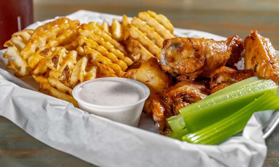 A plate of chicken wings, waffle fries, and celery with ranch 