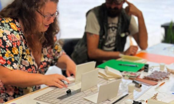 Two individuals at a table, participating in a hands-on activity with paper, tools, and craft supplies