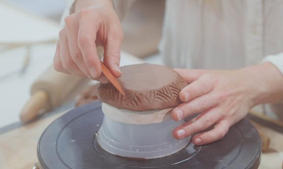 Hands carving patterns into a clay disc