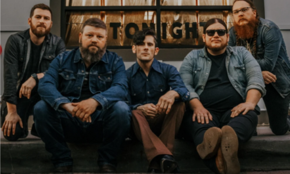 Bandmates from Ole Lonesome pose in denim jackets in front of a building. 