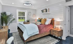 The master bedroom in this vacation rental has white and grey walls and a warm red cover on the wooden bed