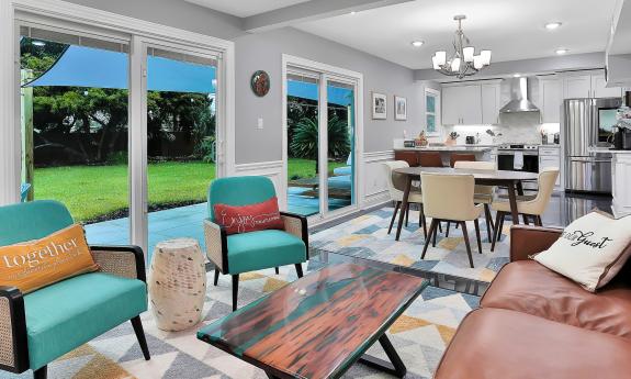 A view of the great room, with seating, dining, and kitchen, all overlooking the back deck and lawn