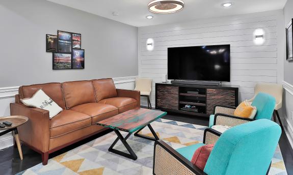 The seating area in the great room has a television, tables, bright-colored aqua chairs and a large sofa