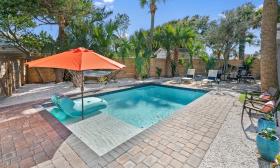 The paved patio, pool, and bright orange shade umbrella at a rental property offered by Euphoria Vacation Homes