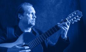 Jonathan Dotson playing his classical guitar against a blue background and under a blue light.