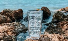 A clear tumbler cup placed on top of a rock at the beach