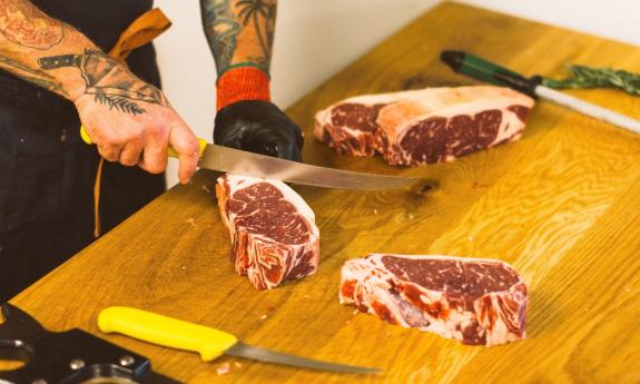 A butcher slicing raw steaks on a wooden cutting board with garnish nearby