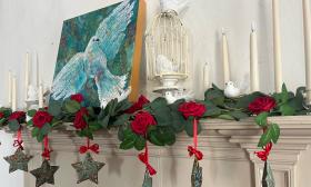 A beige mantle deocrated with candles, roses, and star shaped ornaments. A painting of a dove acts as the centerpiece.