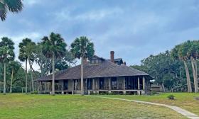 Viewed from Pellicer Creek and surrounded by palm trees, the historical lodge at Princess Place is a wooden structure with a wrap around porch.