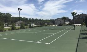 Outdoor tennis courts at San Salito with green surfaces and white lines, enclosed by a fence with homes and trees in the background