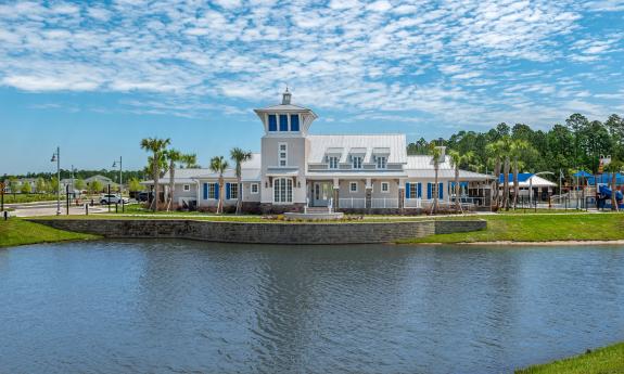 A waterfront clubhouse with a playground and palm trees under a blue sky