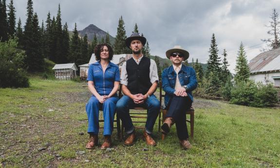 Bandmates from Stillhouse Junkies pose on a bench in front of a group of houses and trees. 