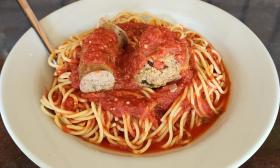 A pasta dish topped with a meatball and sausage
