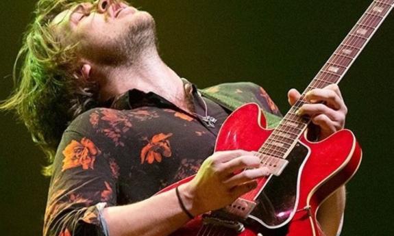 Jackson Stokes sings while playing his guitar on stage for fans. 