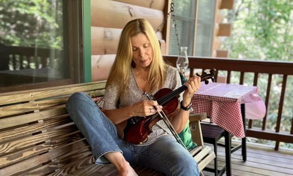 Sue Seymour Westcott playing her fiddle in a porch swing. 