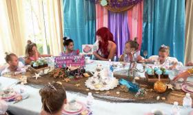 Ariel, from The Little Mermaid, reading to a table of girls dressed up as princesses