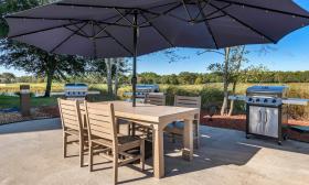A patio with a table under the sun umbrellas and a grill next to the golf course