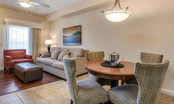 A maroon and beige living room and dining room area with couch, chair, ottoman, table and four chairs