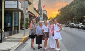 Five women stand on King street at sunset, in front of Bourbon and Boards on a Spirits Tour.