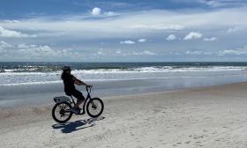 A lone woman bikes along a deserted beach, during a sunny and windy day