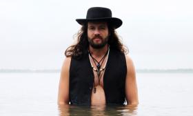 Musician Vern Daysel standing in waist-deep water, with black hat