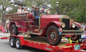 People on an antique firetruck atop a trailer, wave to the crowds in the Easter parade