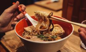 A customer eating a bowl of ramen sprinkled with garnishes and seasonings