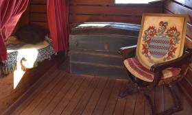 An officer's cabin on the Nao Trinidad is furnished with a trunk, comfortable chair, and bed