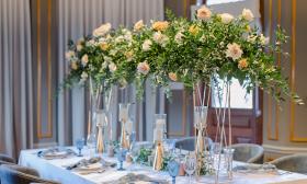 The head table at a wedding reception features tall, slender vases with flowers soaring above 