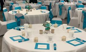 Round tables at a wedding reception with white cloths and teal decorations