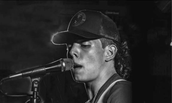 Singer-songwriter Cam Wheaton playing guitar and singing on stage, in a dark ball cap.