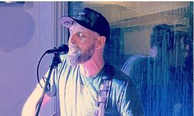 Cover artist Craig Smith in a ball cap and beard, singing in front of microphone
