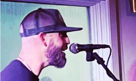 Musician Craig Smith, in ballcap and beard, singing into microphone