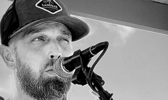 Musician Craig Smith, in ballcap and beard, singing into microphone